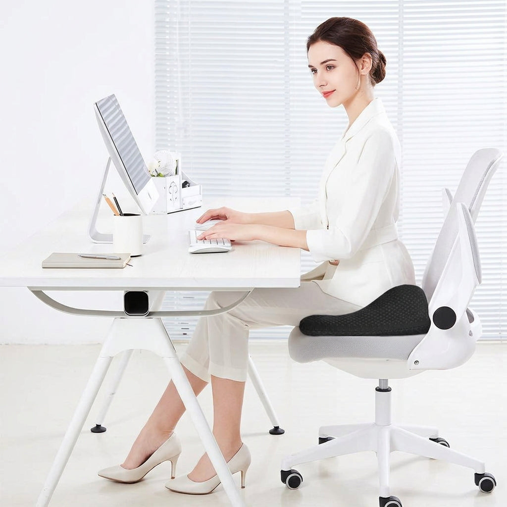 Promotional graphic for a lumbar support cushion, showing a woman sitting at a desk wearing the cushion. The left side lists pain-relief benefits for coccyx, sciatica, tailbone, prostate, hip & pelvis, and lower back.